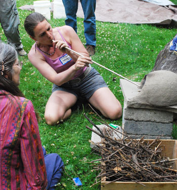 Cecile Green blows air through a metal tube to start a fire in an earth oven at the July 19 Reskilling Festival.